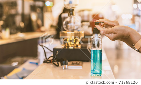Hands of woman pressed blue alcohol gel bottle to prevent the spreading of the Coronavirus (Covid-19) before entrance to coffee shop. New normal lifestyle. Selective focus on alcohol gel bottle. Hands of woman pressed blue alcohol gel bottle to prevent the spreading of the Coronavirus (Covid-19) before entrance to coffee shop. New normal lifestyle. Selective focus on alcohol gel bottle. 71269120
