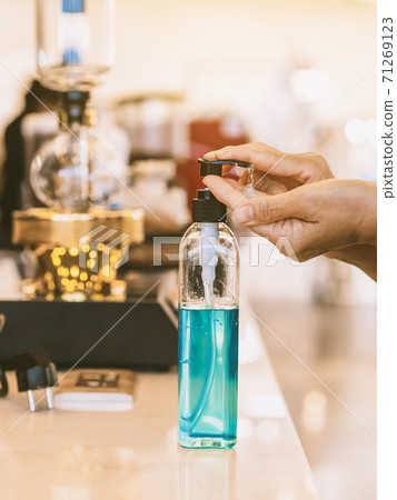 Hands of woman pressed blue alcohol gel bottle to prevent the spreading of the Coronavirus (Covid-19) before entrance to coffee shop. New normal lifestyle. Selective focus on alcohol gel bottle. Hands of woman pressed blue alcohol gel bottle to prevent the spreading of the Coronavirus (Covid-19) before entrance to coffee shop. New normal lifestyle. Selective focus on alcohol gel bottle. 71269123