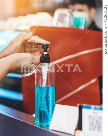 Hands of woman pressed blue alcohol gel bottle to prevent the spreading of the Coronavirus (Covid-19) before entrance to coffee shop. New normal lifestyle. Selective focus on alcohol gel bottle. Hands of woman pressed blue alcohol gel bottle to prevent the spreading of the Coronavirus (Covid-19) before entrance to coffee shop. New normal lifestyle. Selective focus on alcohol gel bottle. 71269125