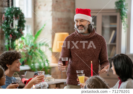 Happy mature man in Santa cap making toast during family dinner by festive table 71270201