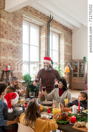 Mature man in Santa cap standing by wife during family dinner by festive table 71270202