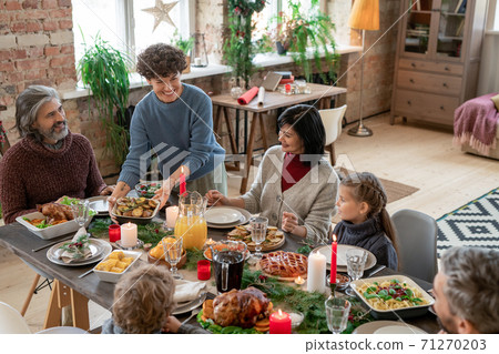 Young cheerful brunette woman putting roasted potatoes on served festive table 71270203