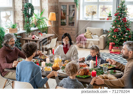 Large family consisting of three generations praying by served festive table 71270204