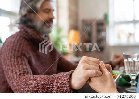 Hands of mature bearded man with closed eyes and his wife praying before dinner 71270206