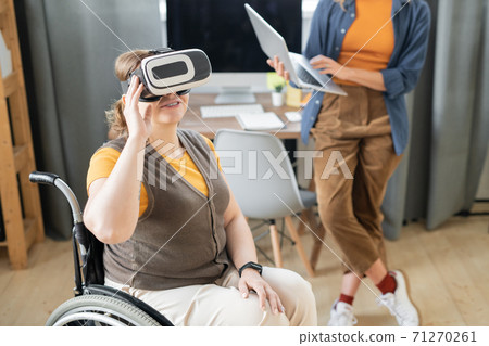 Disable businesswoman in vr headset sitting in wheelchair against busy colleague 71270261