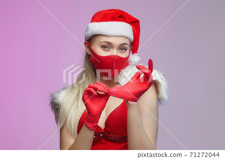 young girl in a Santa hat and a mask, puts red gloves on her hands. Christmas and COVID-19 prevention concept young girl in a Santa hat and a mask, puts red gloves on her hands. Christmas and COVID-19 prevention concept 71272044