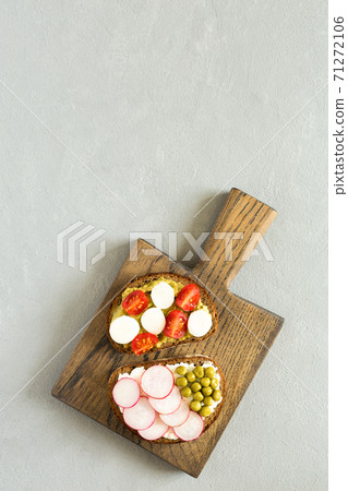 Two vegetable sandwiches on slices of dark bread with radish, cucumber, cherry tomatoes on a wooden cutting board flat lay on gray concrete background with copy space. 71272106