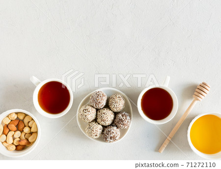 Homemade raw candy energy balls with almond, cashews, peanut butter and hazelnuts on the plate with tea cups flat lay on gray background with copy space. Organic snack. Vegetarian food. 71272110