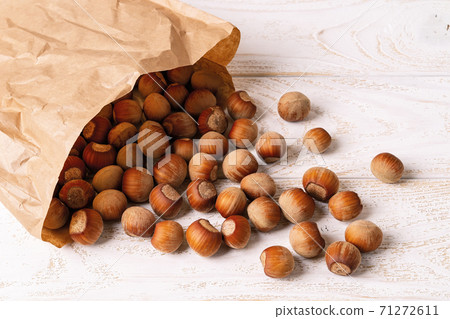 Unpeeled hazelnuts spilled out of a paper bag onto the white wood table. Unpeeled hazelnuts spilled out of a paper bag onto the white wood table. 71272611