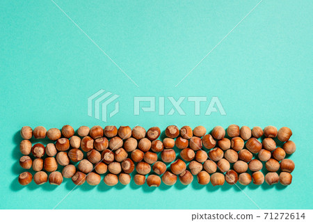 Strip of unpeeled hazelnuts casts shadows on a turquoise paper background. Strip of unpeeled hazelnuts casts shadows on a turquoise paper background. 71272614