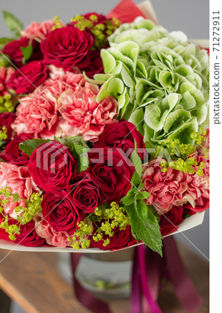 Red and green flowers. Autumn bouquet of mixed flowers in glass vase on wooden table. The work of the florist at a flower shop. Fresh cut flower. Red and green flowers. Autumn bouquet of mixed flowers in glass vase on wooden table. The work of the florist at a flower shop. Fresh cut flower. 71272911