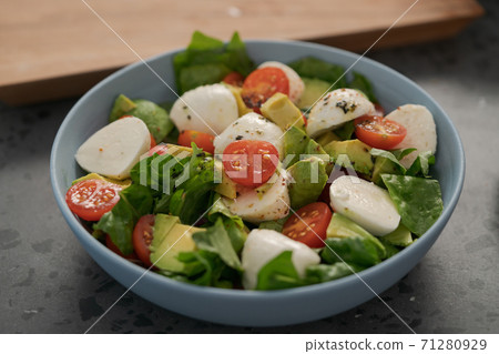 Salad with avocado, cherry tomatoes, romaine and mozzarella in blue bowl on concrete countertop Salad with avocado, cherry tomatoes, romaine and mozzarella in blue bowl on concrete countertop 71280929