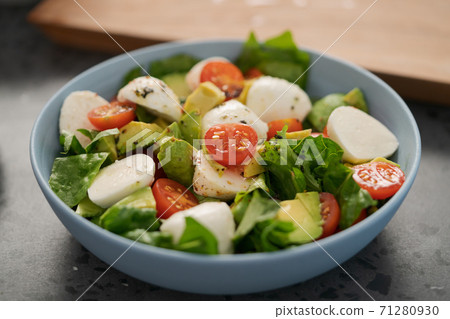 Salad with avocado, cherry tomatoes, romaine and mozzarella in blue bowl on concrete countertop Salad with avocado, cherry tomatoes, romaine and mozzarella in blue bowl on concrete countertop 71280930