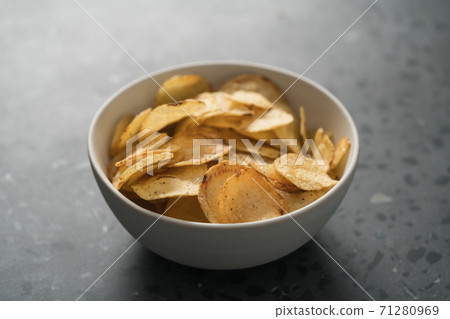 Organic potato chips with black pepper in white ceramic bowl on concrete background Organic potato chips with black pepper in white ceramic bowl on concrete background 71280969