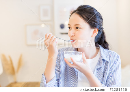 Young woman eating yogurt at home 71281536