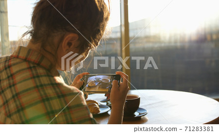 Close up of woman holds modern smartphone and taking pictures of her morning breakfast coffee and tasty croissant buns to share photos on social media resources 71283381