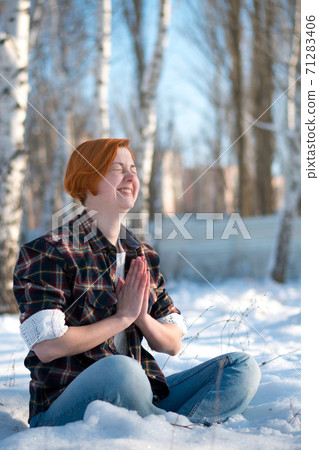 Cute ginger girl meditates in winter forest. 71283406