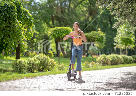 Long-haired young girl riding a scooter in the park and looking happy 71285825