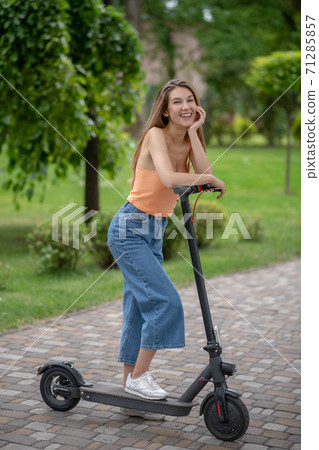 Long-haired cute girl resting on her scooter and smiling 71285857