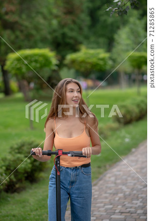 Long-haired cute girl with a scooter in the park 71285865