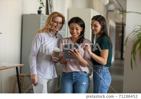 Smiling diverse female colleagues standing at office hall using pad 71286452
