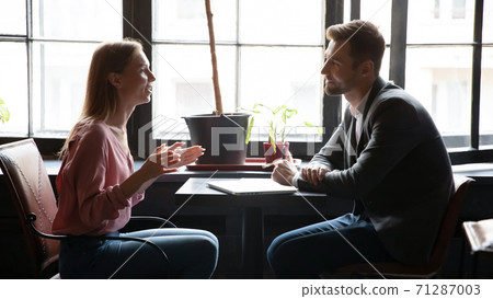 Diverse millennial partners discussing startup details at table in cafe Diverse millennial partners discussing startup details at table in cafe 71287003