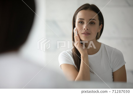 Pretty young lady cleansing face with lotion using cotton disc Pretty young lady cleansing face with lotion using cotton disc 71287030