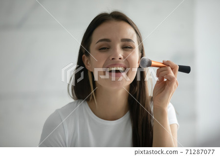 Laughing young female putting powder on face using makeup brush Laughing young female putting powder on face using makeup brush 71287077