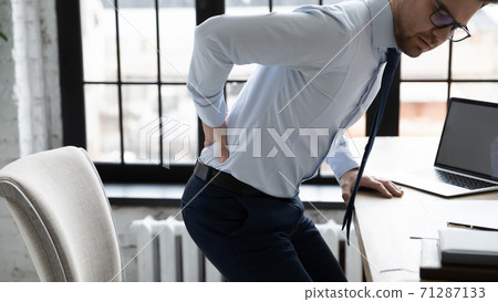 Unhealthy young office worker having painful feelings in lower back. Unhealthy young office worker having painful feelings in lower back. 71287133