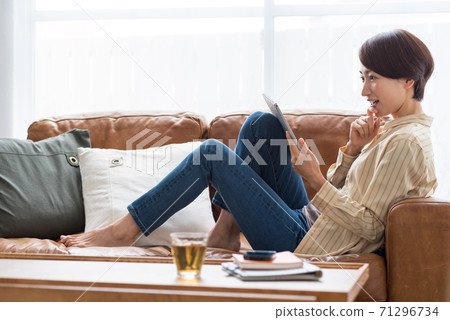 一名中年婦女坐在沙發上,在平板電腦上觀看視頻時休息 一名中年婦女坐在沙發上,在平板電腦上觀看視頻時休息 71296734
