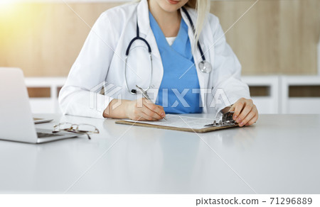 Unknown woman-doctor at work filling up medication history record form in sunny clinic, close-up 71296889