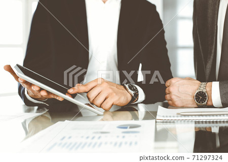 Business people using tablet computer while working together in modern office. Unknown businessman sitting at the desk with his colleague or partner. Teamwork and partnership concept Business people using tablet computer while working together in modern office. Unknown businessman sitting at the desk with his colleague or partner. Teamwork and partnership concept 71297324
