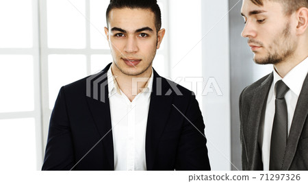Two businessmen or partners working with tablet computer at the desk in modern office. Headshot of arab male entrepreneur or manager with colleague at workplace. Multi ethnic teamwork, partnership and Two businessmen or partners working with tablet computer at the desk in modern office. Headshot of arab male entrepreneur or manager with colleague at workplace. Multi ethnic teamwork, partnership and 71297326