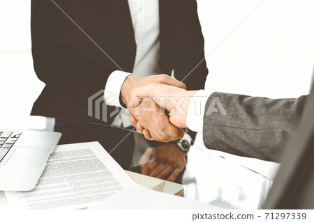 Unknown diverse business people are shaking hands finishing up meeting at the desk in office, close-up. Handshake concept Unknown diverse business people are shaking hands finishing up meeting at the desk in office, close-up. Handshake concept 71297339
