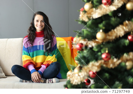 Young beautiful lesbian woman smiling and siting on couch near christmas tree 71297749