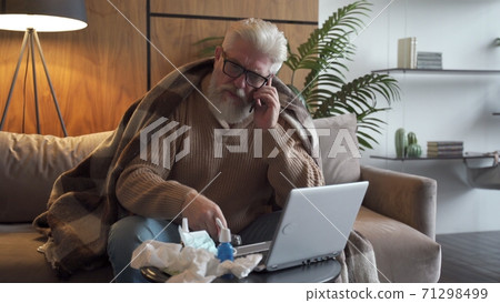 A sick elderly person calls the doctor on the phone. A man is ill and is sitting on the couch at home A sick elderly person calls the doctor on the phone. A man is ill and is sitting on the couch at home 71298499