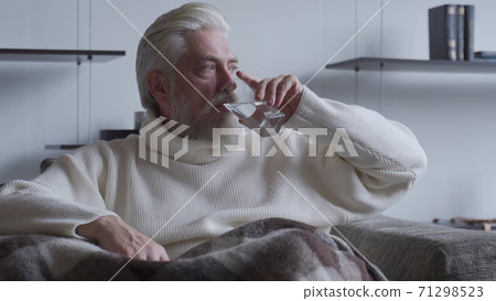 Elderly man with a gray beard is sitting in a chair and drinking a glass of water Elderly man with a gray beard is sitting in a chair and drinking a glass of water 71298523