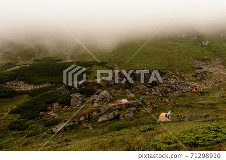 A small tent town in the mountains, tents by the lake in the mountains, the area near the lake Brebeneskul, the Carpathian mountains, fog and rain in the mountains. 71298910