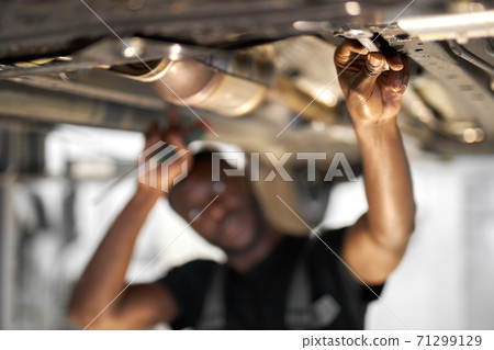 young african male car mechanic in uniform checking car in automobile service with lifted vehicle, focus on hands young african male car mechanic in uniform checking car in automobile service with lifted vehicle, focus on hands 71299129