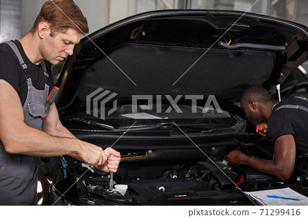 two diverse auto mechanics cooperating while examining car engine performance in auto repair shop two diverse auto mechanics cooperating while examining car engine performance in auto repair shop 71299416