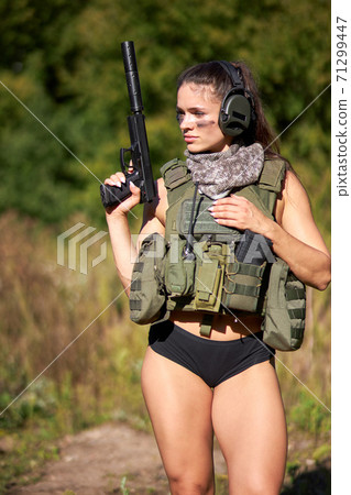 young caucasian athletic female in short top and shorts holding gun posing in forest 71299447