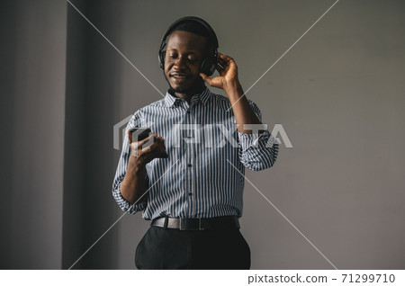Young african man listening to music with wireless earphones and dancing at home 71299710