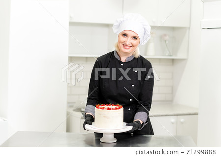Portrait of friendly smiling female professional confectioner topping a cupcake with cream using a pastry bag 71299888
