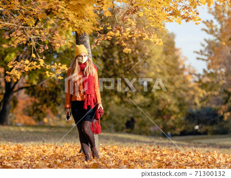 Worried woman checking her phone wearing mask in fall 71300132
