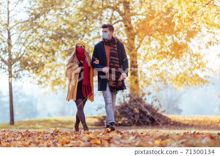 Couple wearing mask walking in autumn park 71300134