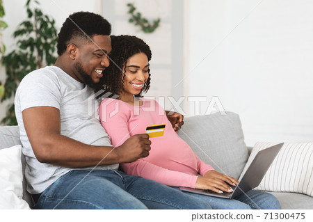 Happy african american expecting family using laptop, shopping online 71300475