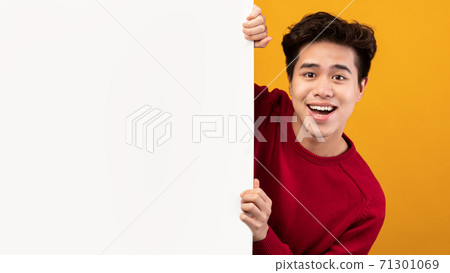 Asian guy hiding behind blank white advertising billboard 71301069