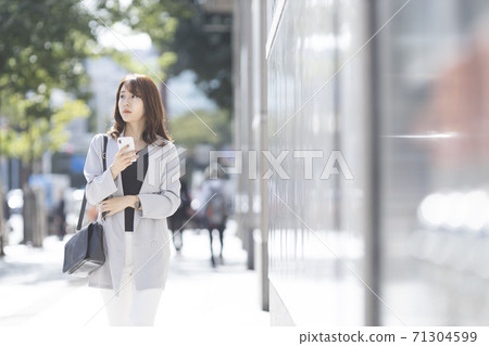 A young woman walking with a smartphone outdoors 71304599