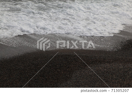 Small waves crashing against the black sand beach 71305207