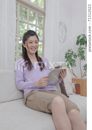 Woman holding a tablet PC on the sofa 71312023